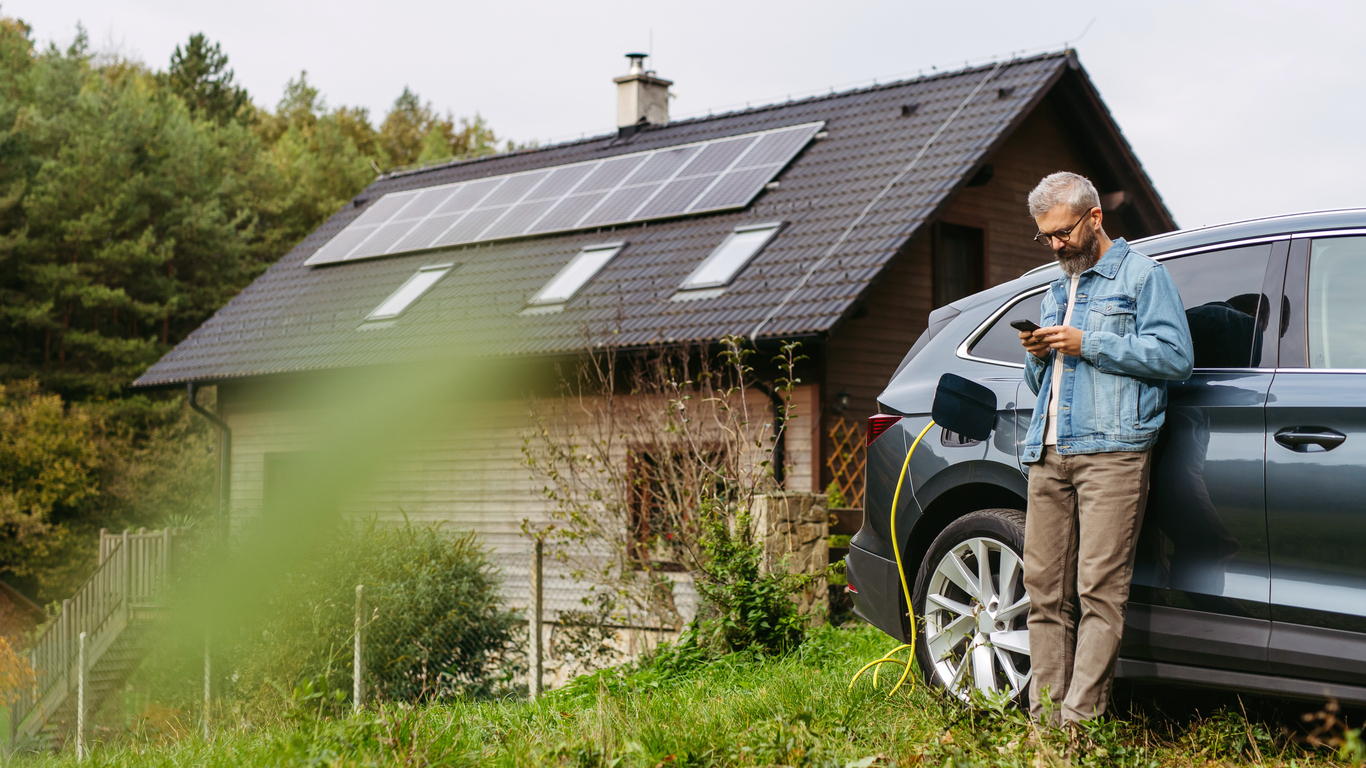 Man charging e-vehicle in front of house with solar panels