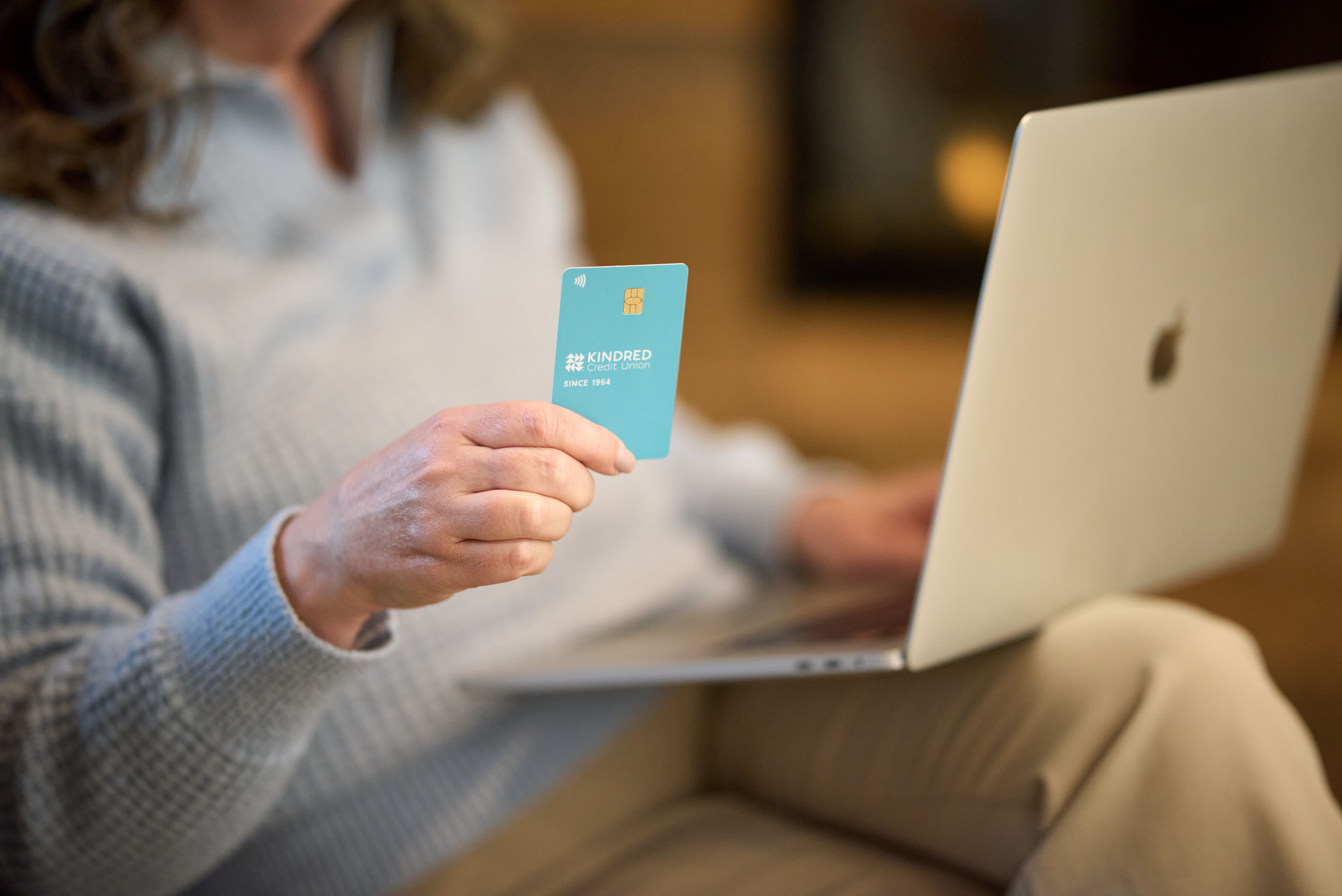 Member holding a Kindred debit card while working on a laptop