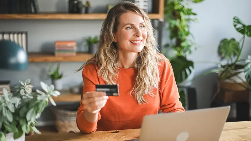 Smiling woman with orange sweater holding a credit card
